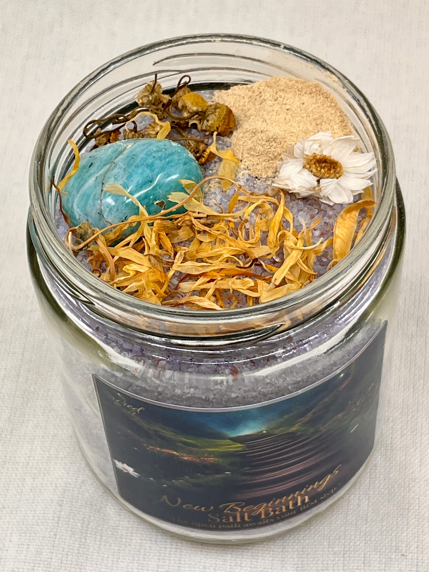 Glass jar with bath salts, flowers, and a blue stone on a light background
