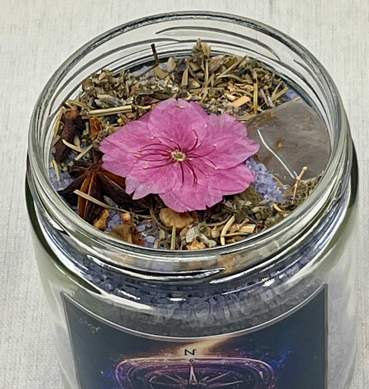 Glass jar with dried herbs and a pink flower on a textured surface