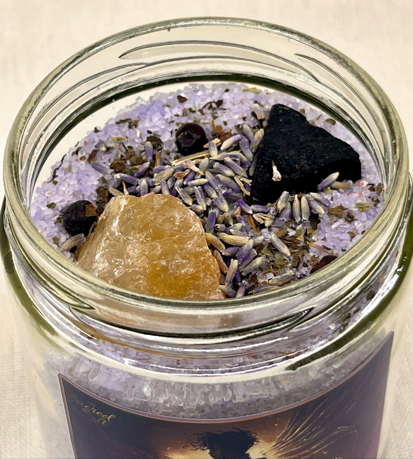 Glass jar with lavender, black stones, and a brown crystal on a light background