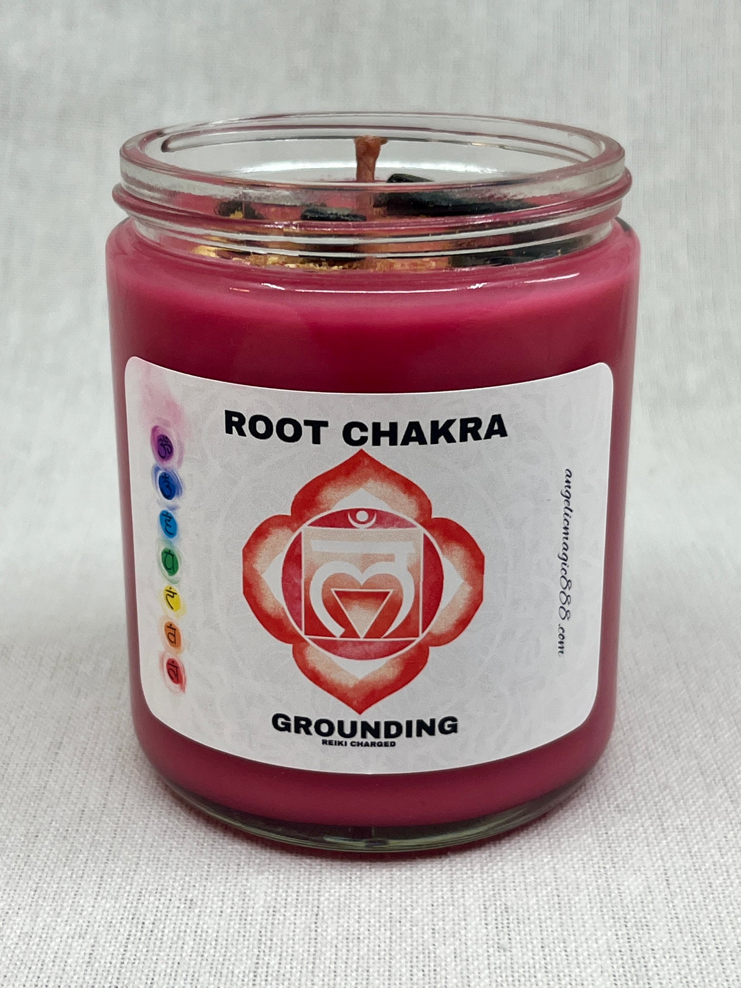 Red candle in a glass jar with a label indicating 'Root Chakra' and 'Grounding'.