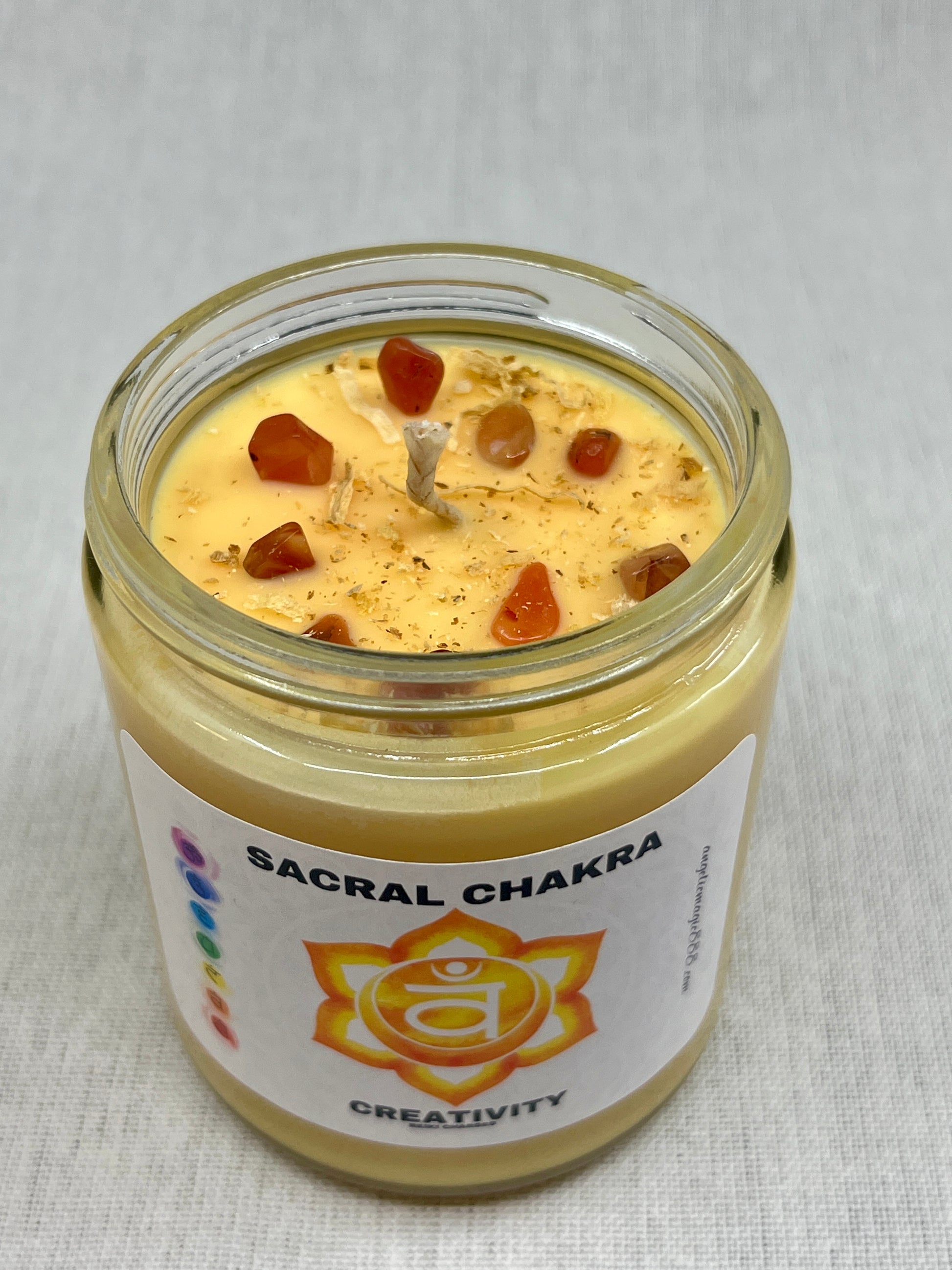 Candle in a glass jar labeled 'Sacral Chakra' with a white background