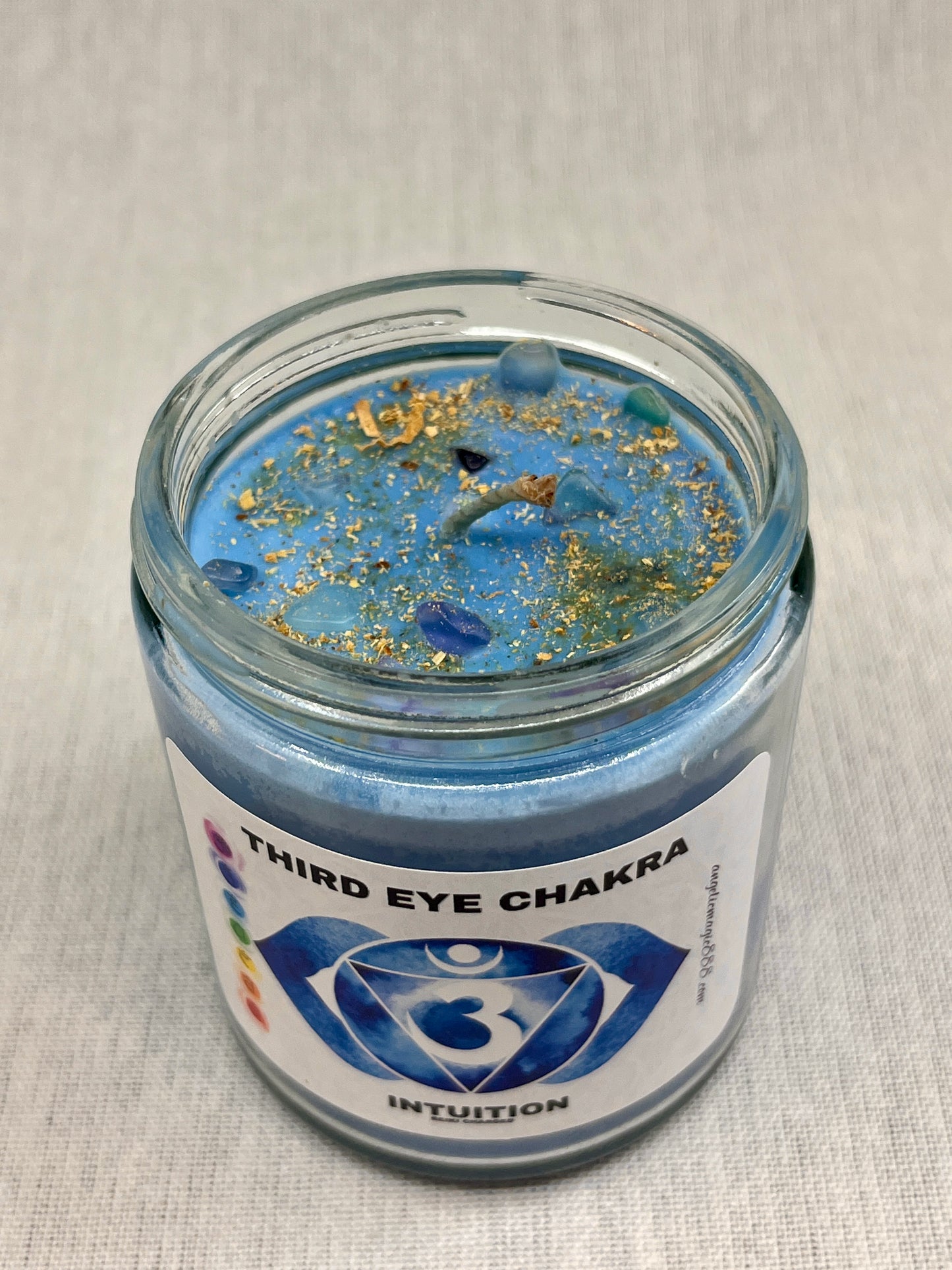 Blue candle in a glass jar labeled 'Third Eye Chakra Intuition' on a light gray background
