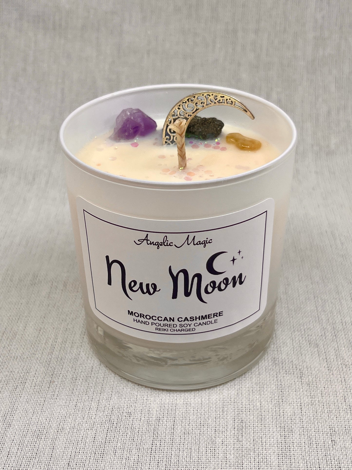Candle in a glass jar labeled 'New Moon' with decorative elements on a textured gray background