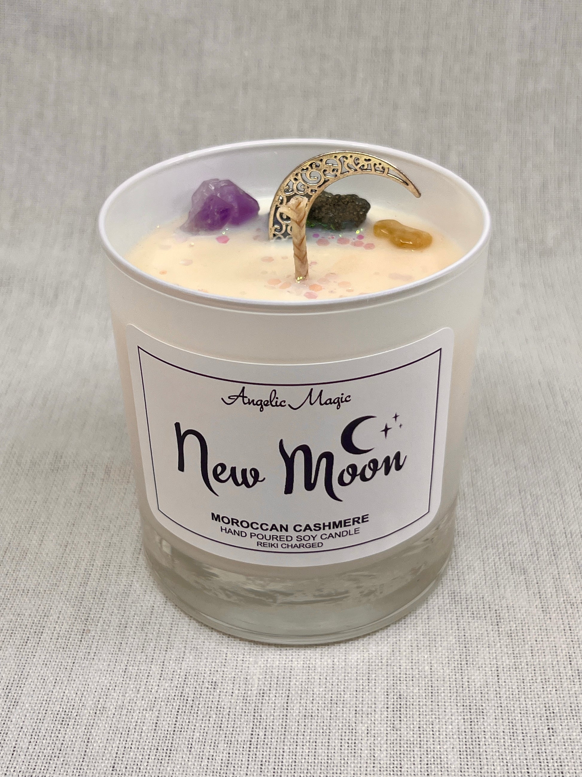 Candle in a glass jar labeled 'New Moon' with decorative elements on a textured gray background