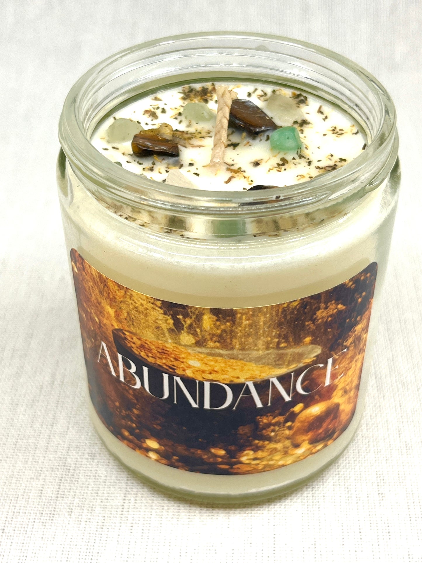 Candle in a glass jar with 'Abundance' label on a white background