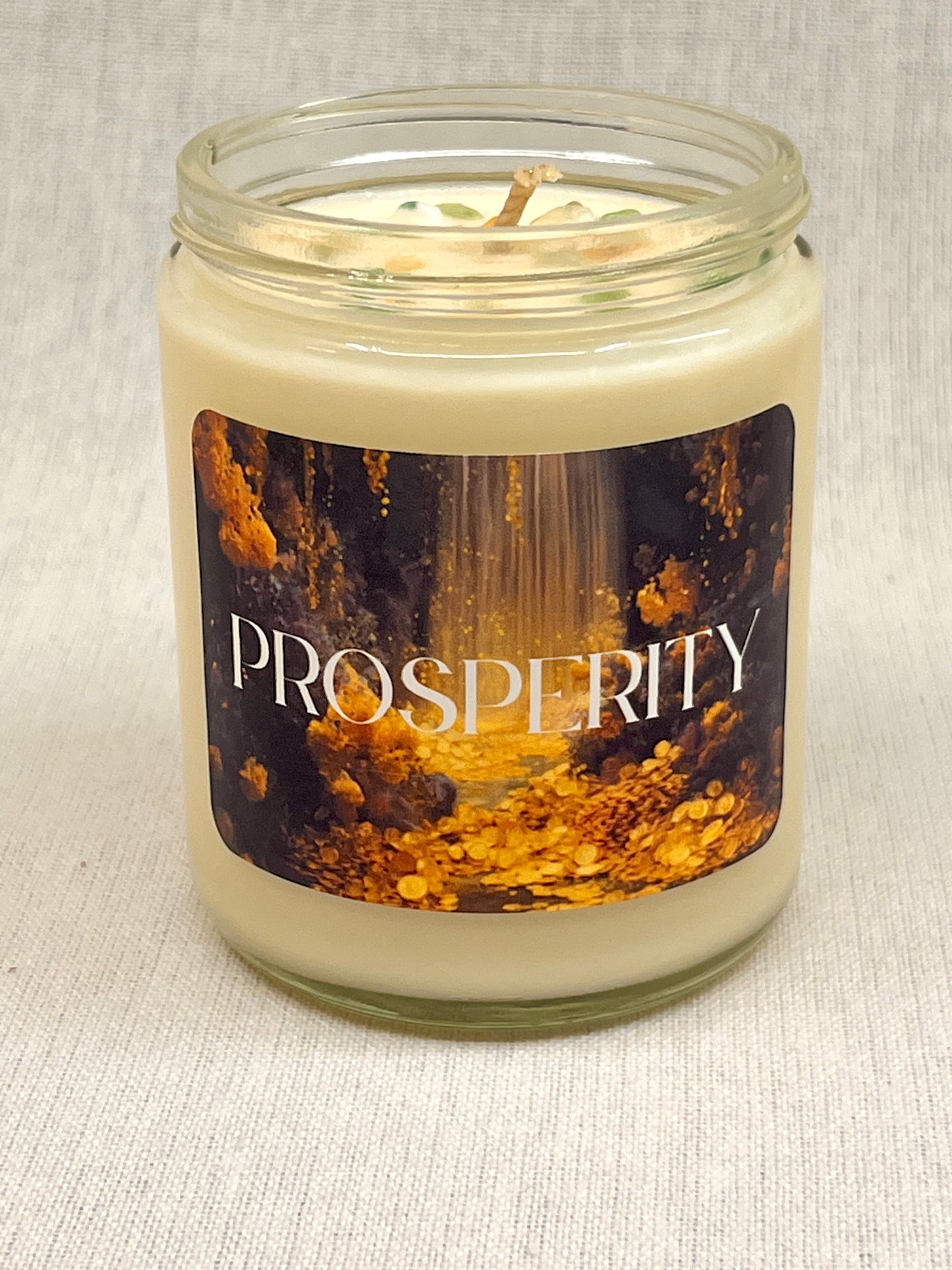 Candle in a glass jar with a 'Prosperity' label on a textured surface