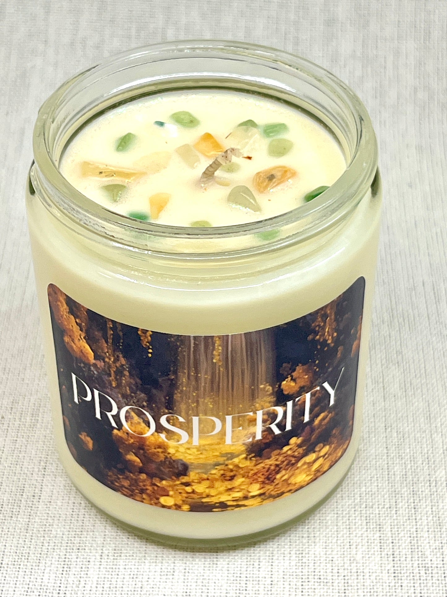 Candle in a glass jar with 'Prosperity' label on a textured surface