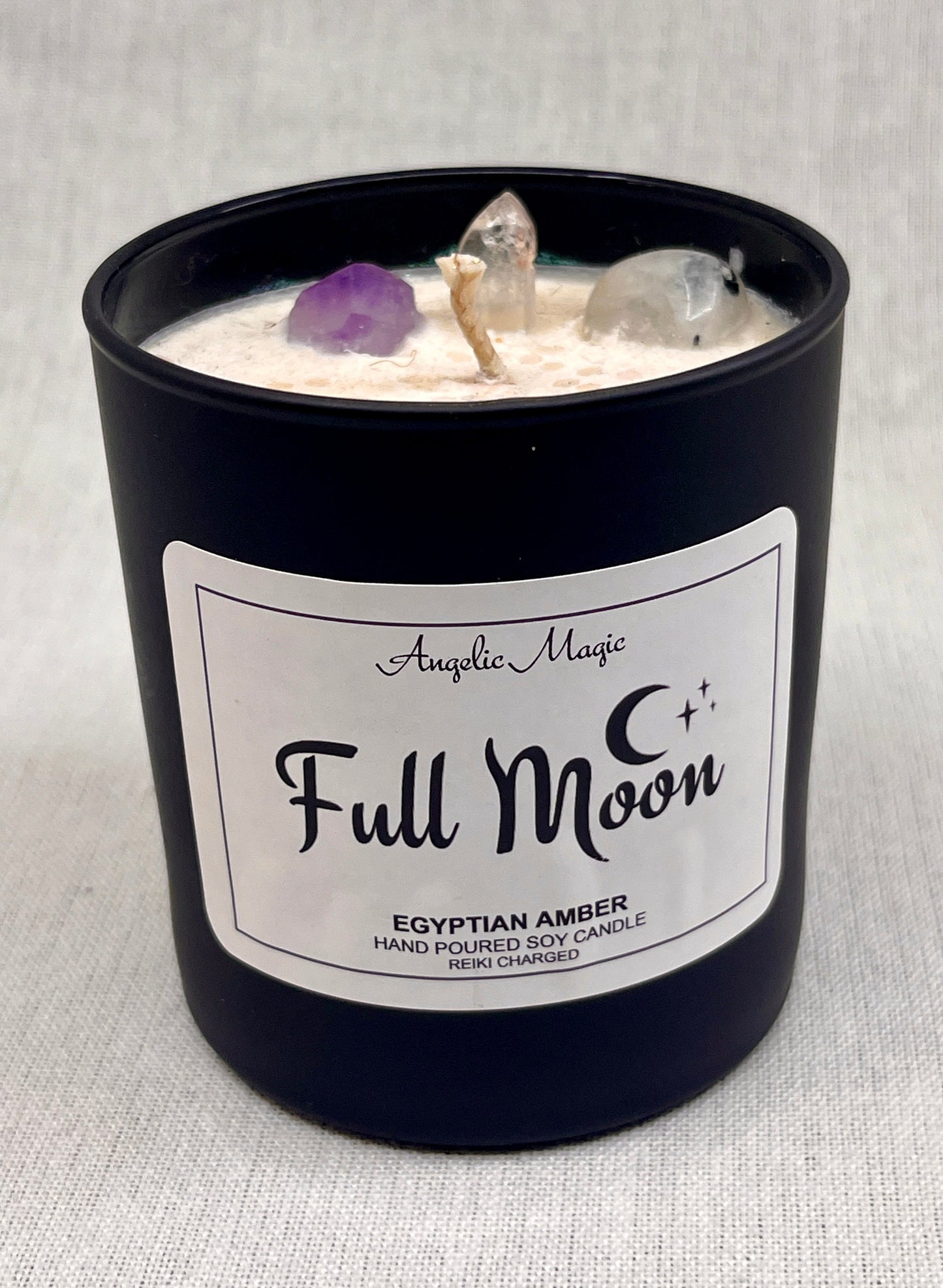 Candle labeled 'Full Moon' with crystals on a gray background