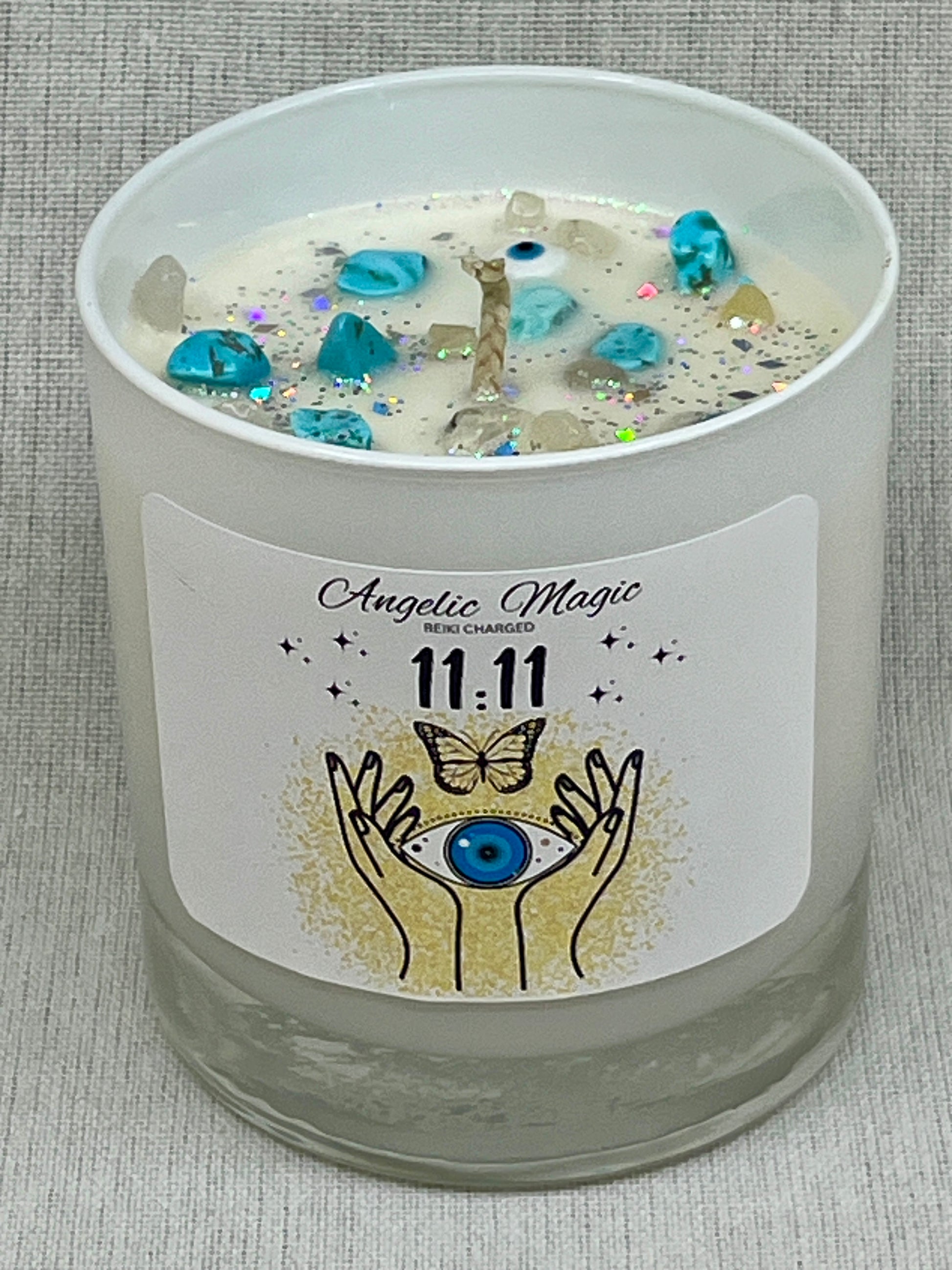 Candle with decorative label featuring hands, butterfly, and eye design on a textured surface.