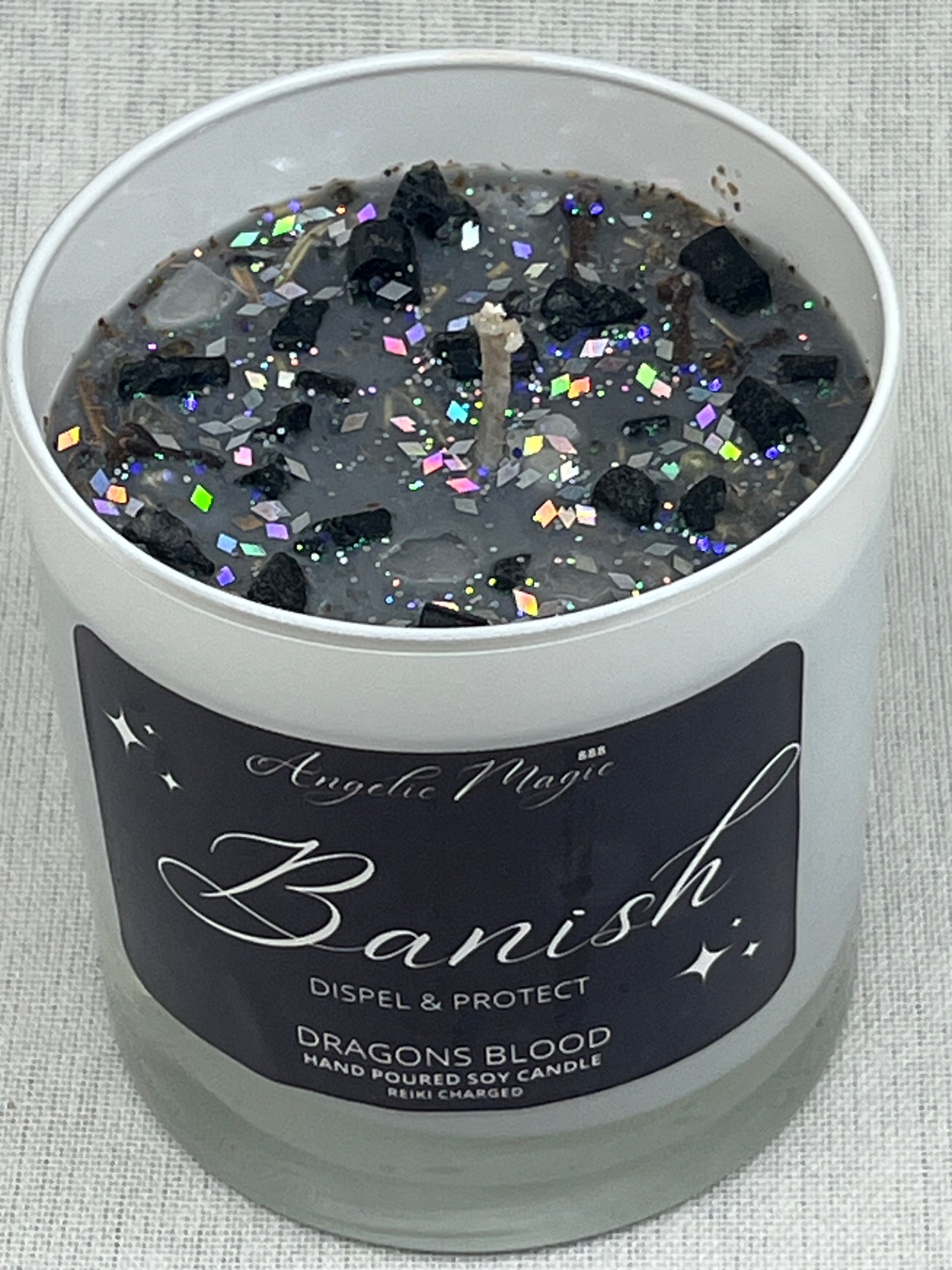 Decorative candle container with 'Banish' label and colorful glitter inside, on a textured surface.