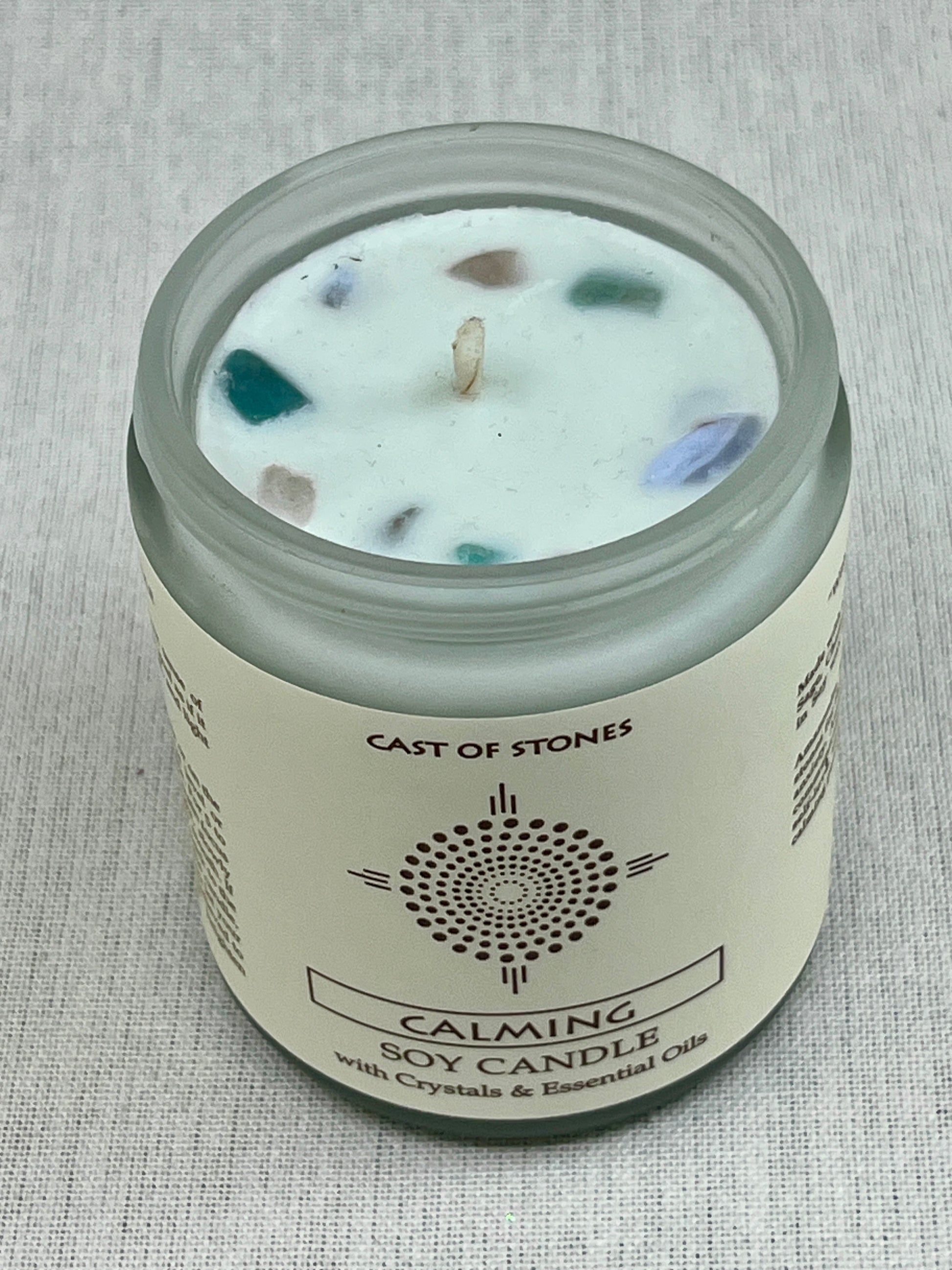 Candle jar labeled 'Cast of Stones' with visible crystals on a textured gray background