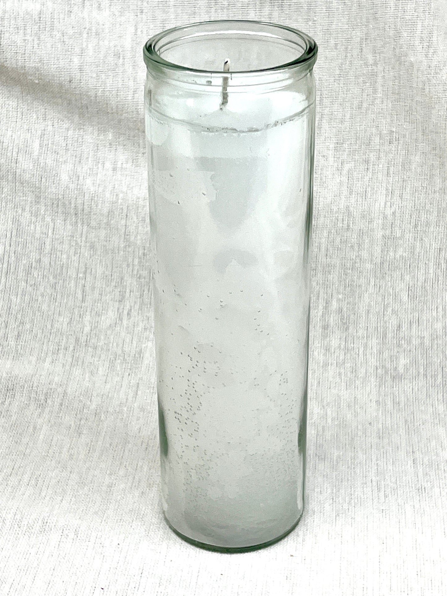 Clear glass candle holder with a candle on a white fabric background