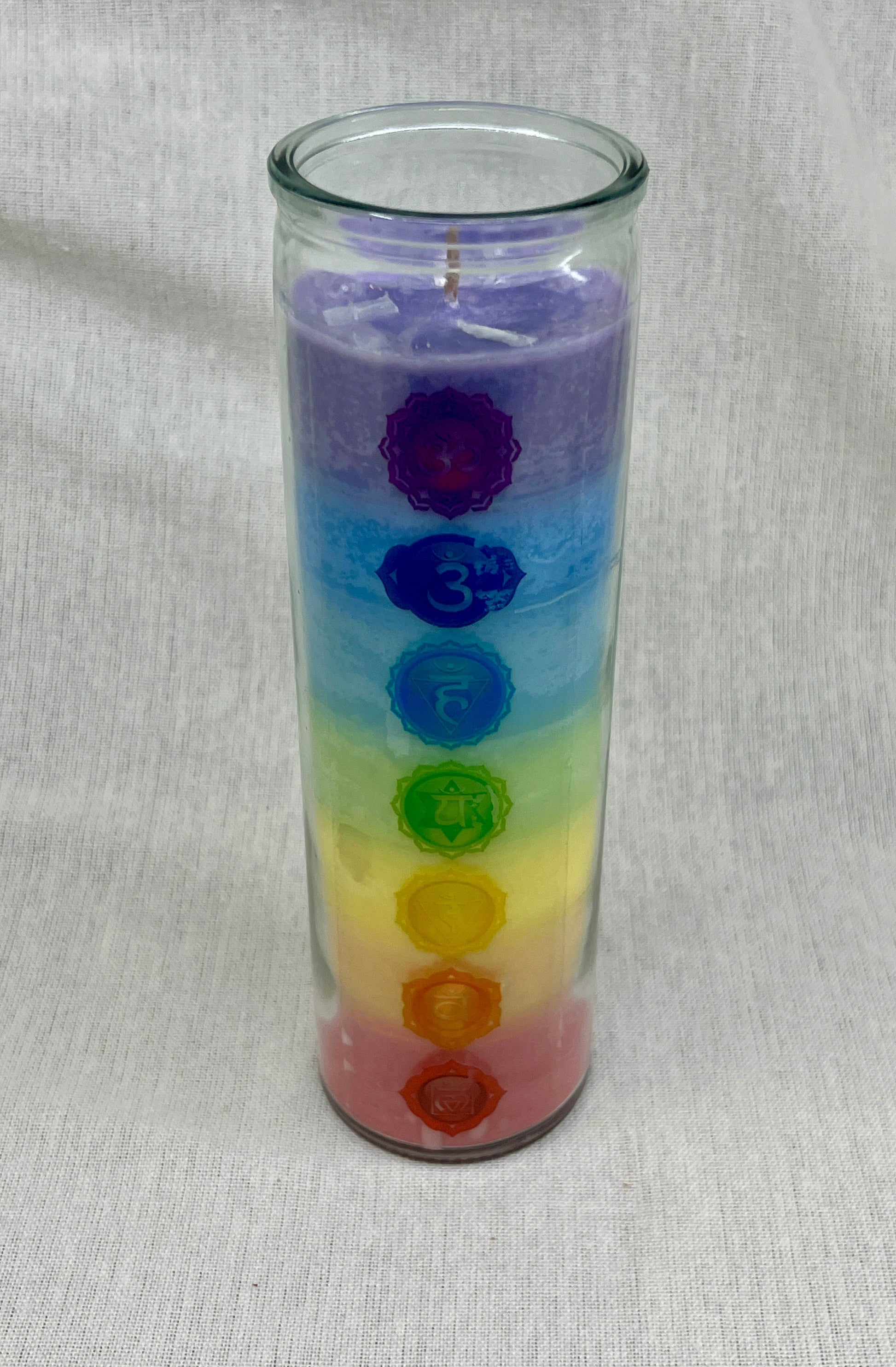 Colorful candle with chakra symbols in a glass container on a light gray background