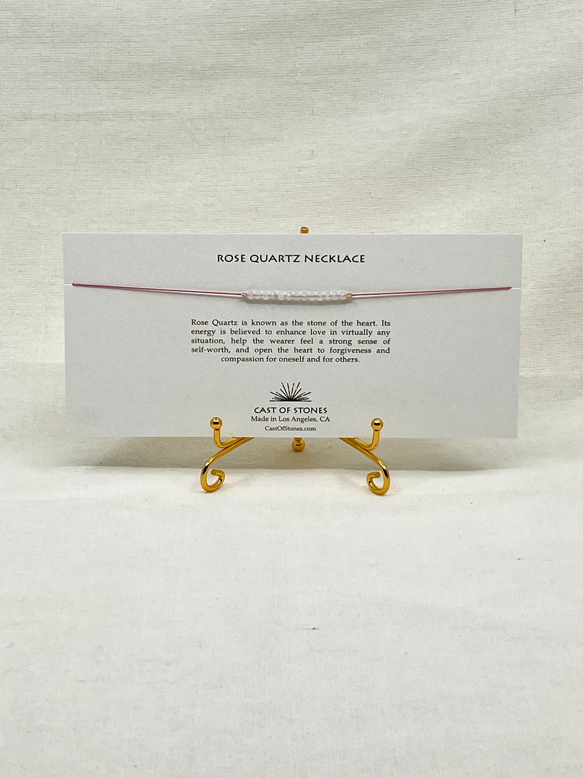 Rose quartz necklace on a display card with gold stands on a white background