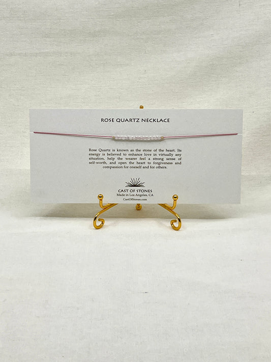 Rose quartz necklace on a display card with gold stands on a white background