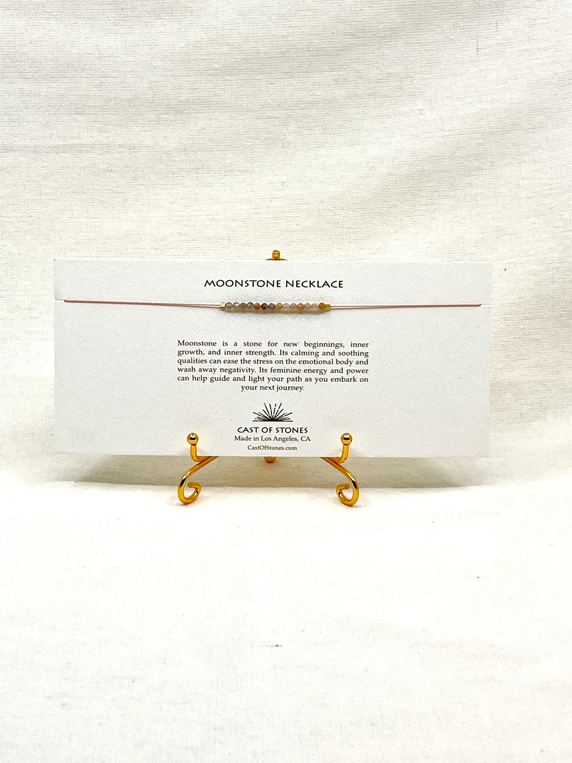 Moonstone necklace on a white card with gold hook, against a textured white background