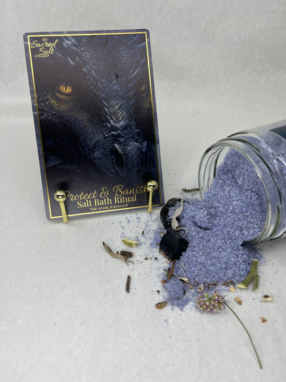 Purple bath salts spilling from a jar onto a black card with gold text on a light gray background