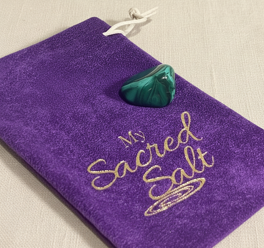 Malachite tumble stone on a purple pouch labeled 'My Sacred Salt' on a cream linen background