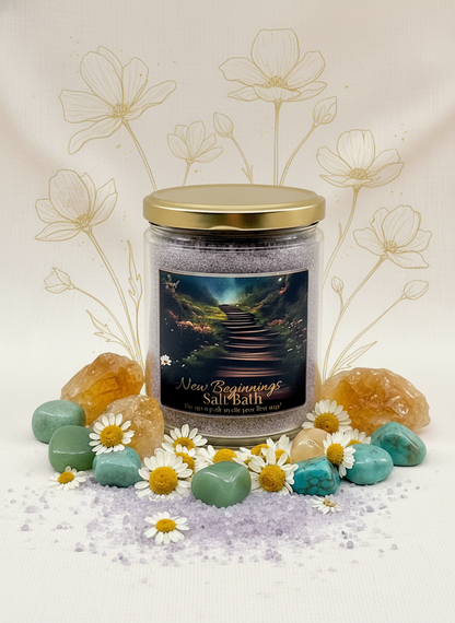 Candle jar labeled 'New Beginnings Salt Bath' with decorative stones, flowers, and a scenic label on a light background.