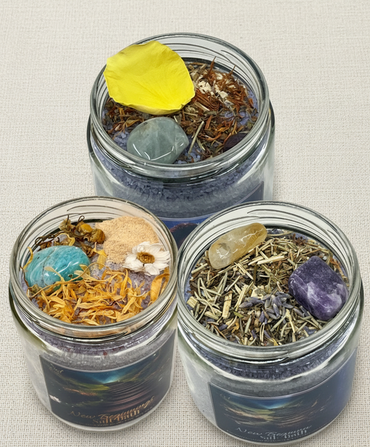 Three glass jars from the release & surrender salt bath collection filled with various herbs, stones, and a yellow floral on a white background
