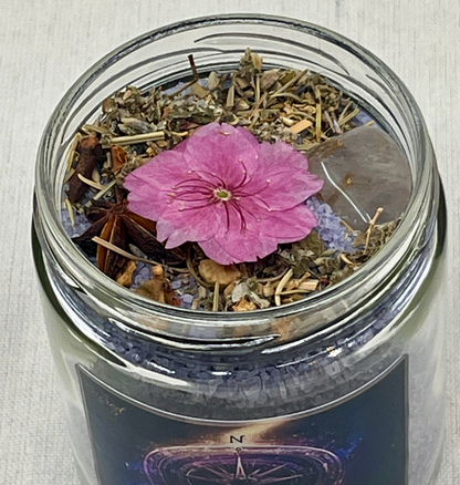 Glass jar with dried herbs and a pink flower on a textured surface