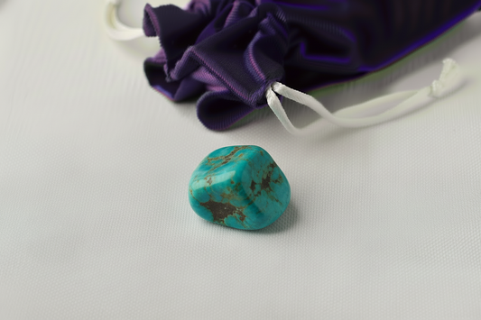 Turquoise stone with a purple drawstring bag on a light gray background
