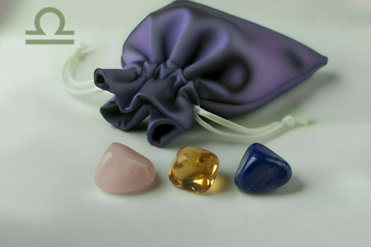 Three gemstones (pink, yellow, blue) in front of a purple drawstring bag on a white background.