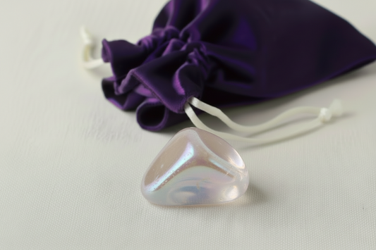 Angel Aura tumble stone on a white surface with a purple drawstring bag in the background.