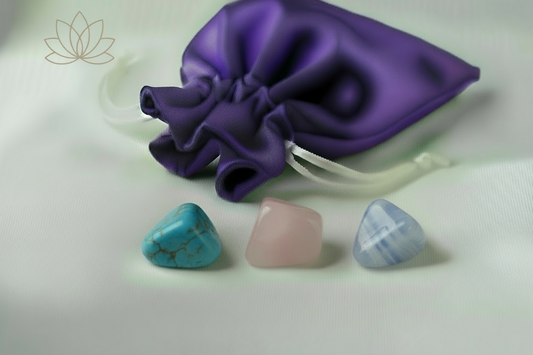 Three crystal stones on a white surface with a purple drawstring bag in the background.