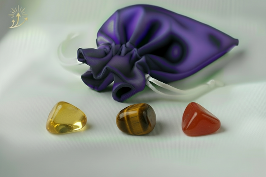 Three colorful gemstones in front of a purple drawstring bag on a white background
