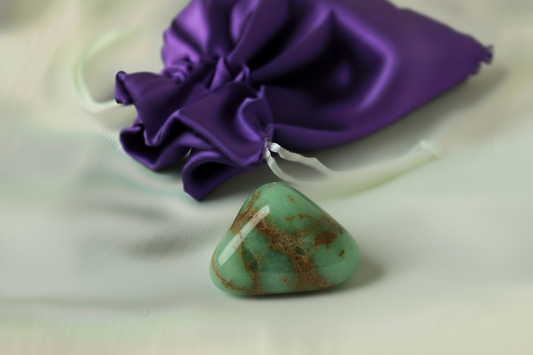 Turquoise stone pendant on a white string with a purple drawstring bag in the background.