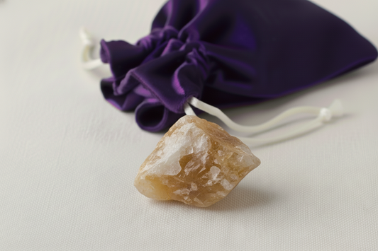 Brown crystal stone on a light gray surface with a purple drawstring bag in the background.