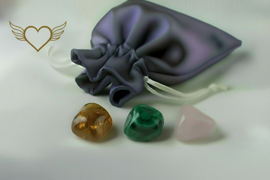 Three crystal stones (amber, green, pink) with a gray drawstring bag on a light background.