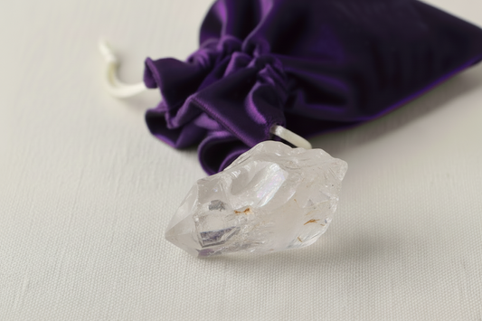 Clear crystal on a light gray surface with a purple drawstring bag in the background