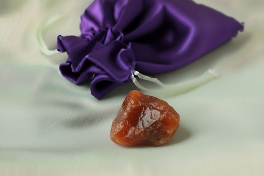 Raw amber stone on a white surface with a purple drawstring bag in the background