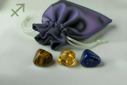 Three crystal stones (brown, yellow, blue) in front of a purple drawstring bag on a white background.
